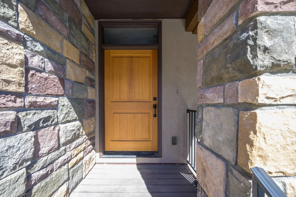 The image showcases the exterior entryway to the townhome, featuring a wooden door framed by a stone wall. The setting is warm and inviting, creating a memorable first impression for arriving guests and highlighting the home's welcoming character.