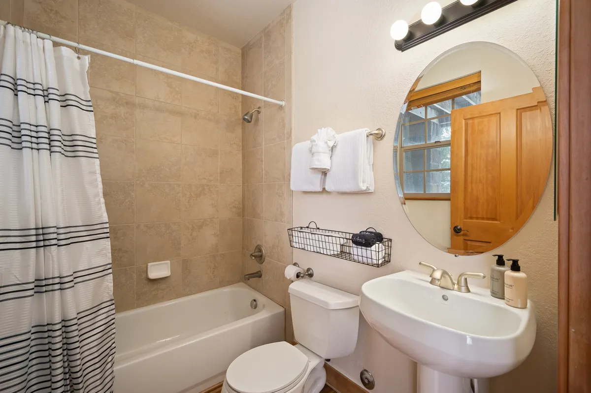 A serene bathroom scene featuring an inviting bathtub, modern sink, large mirror, soft towels, and a wooden door. The soothing design and thoughtful details evoke a spa-like experience, perfect for moments of relaxation and self-care.