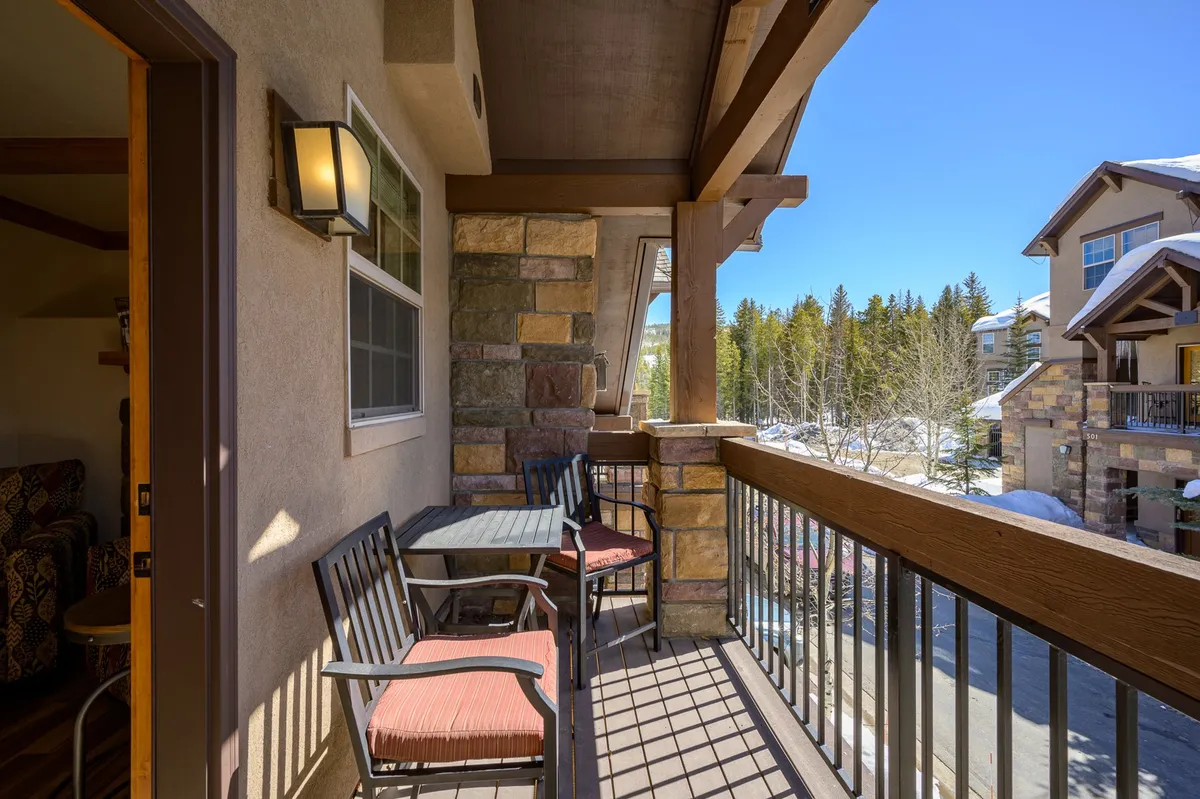 A serene balcony with comfortable seating and stonework overlooking a lush forest, inviting guests to savor a morning coffee or unwind with mountain views.