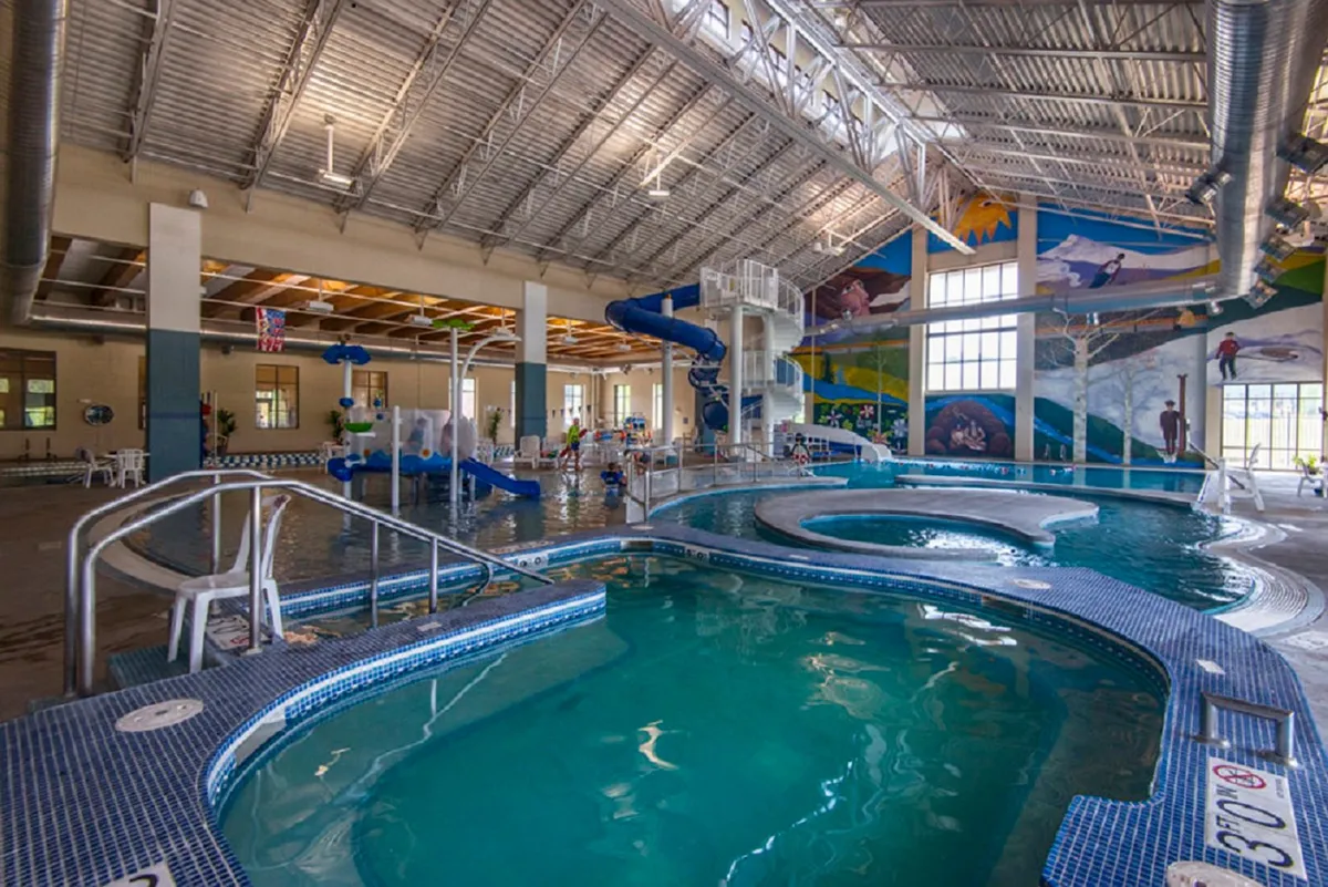 An energetic interior view of a pool area with water slides, colorful murals, and lively seating zones—perfect for families and children. The atmosphere is joyful, suggesting fun and relaxation after days filled with adventure.