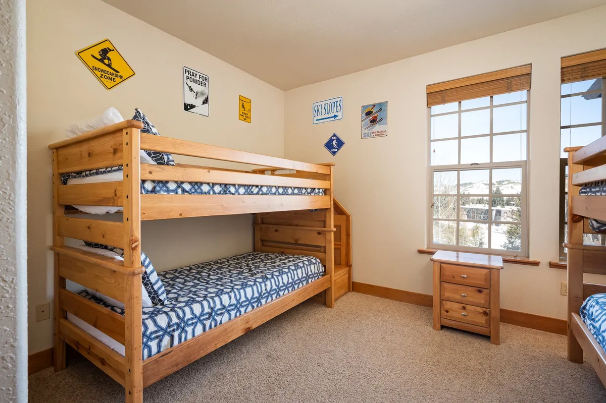 A playful bunkroom with twin-over-twin bunk beds, a window offering a scenic view, and decorative wall signs. The space exudes a fun, inviting vibe ideal for kids or friends to share stories and build memories.