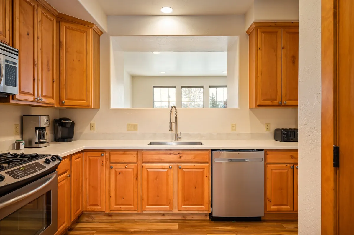 A modern kitchen with a central island, stainless steel appliances, natural wood cabinetry, and large windows that bathe the space in natural light. The setup is ideal for creating meals, gathering with family, and sharing coffee or conversation.