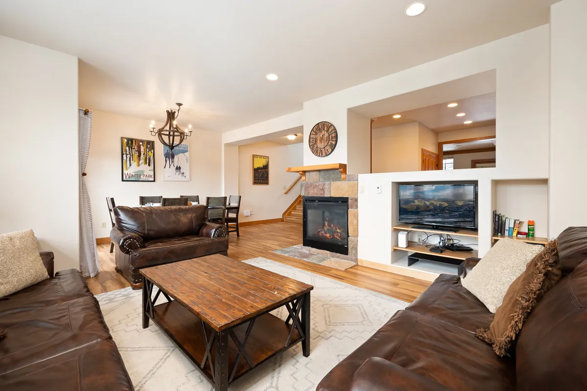 A warmly lit living room featuring leather sofas arranged around a wooden coffee table and a two-sided gas fireplace. Wall art adds a touch of mountain-modern style, and the cozy setup hints at spaces for relaxing, socializing, or catching up on TV.