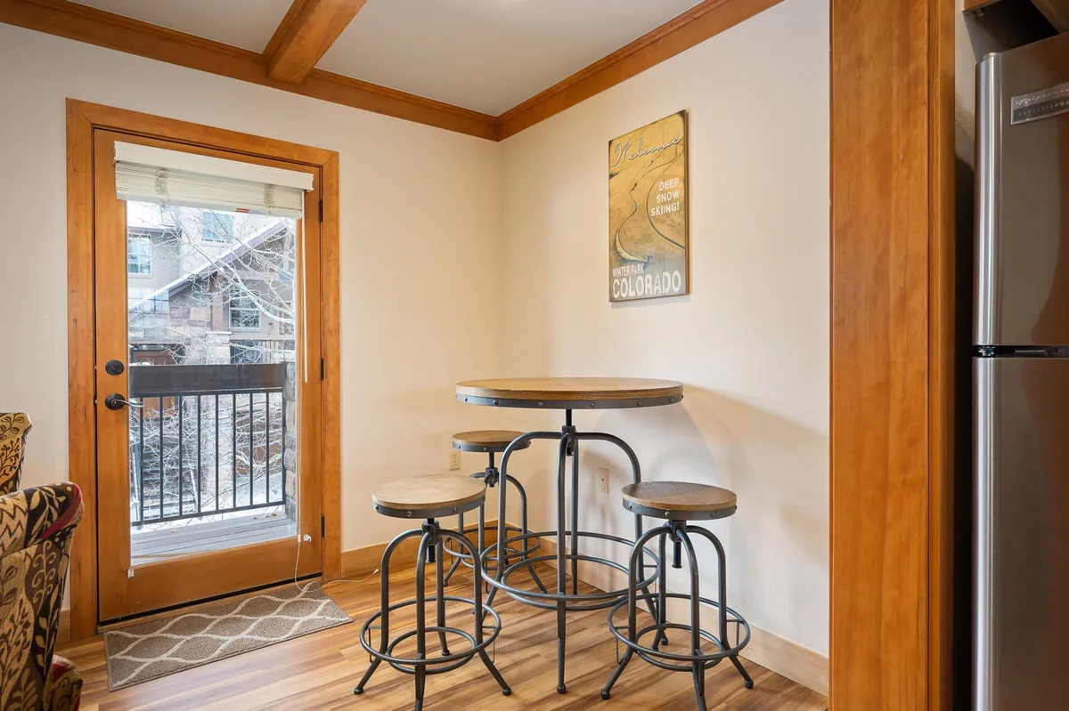 A cozy round table with stools positioned beside a door that offers a glimpse of the outdoors, complemented by wall artwork. The arrangement suggests easy access to outdoor activities and relaxation with scenic views.
