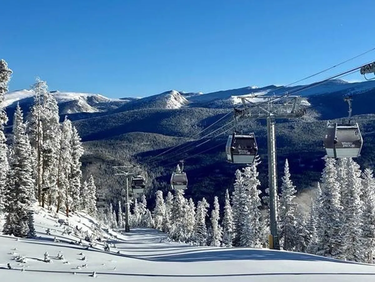 A breathtaking winter landscape featuring a ski lift gliding above snow-covered trees, with a majestic mountain range and a clear blue sky in the background. Guests can easily imagine themselves embarking on skiing, snowboarding, or snowshoeing adventures in this picturesque setting.