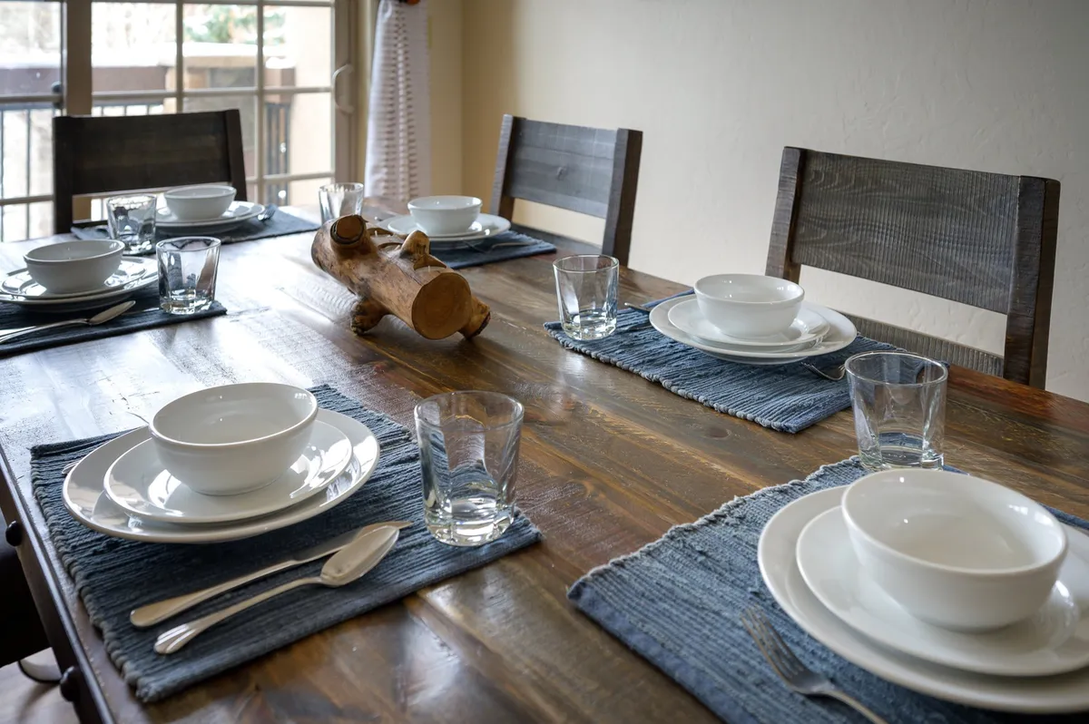 A welcoming dining area centered around a large table with a wooden centerpiece and attractive place settings. The setup feels perfect for shared family meals, board games, and group celebrations, exuding warmth and togetherness.