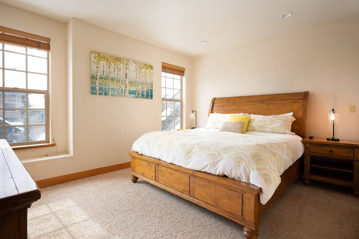 A serene master bedroom featuring a large wooden bed, tasteful decorative artwork on the wall, and a wooden dresser. Soft natural light filters in, creating a cozy and inviting retreat ideal for restful nights or lazy mornings.