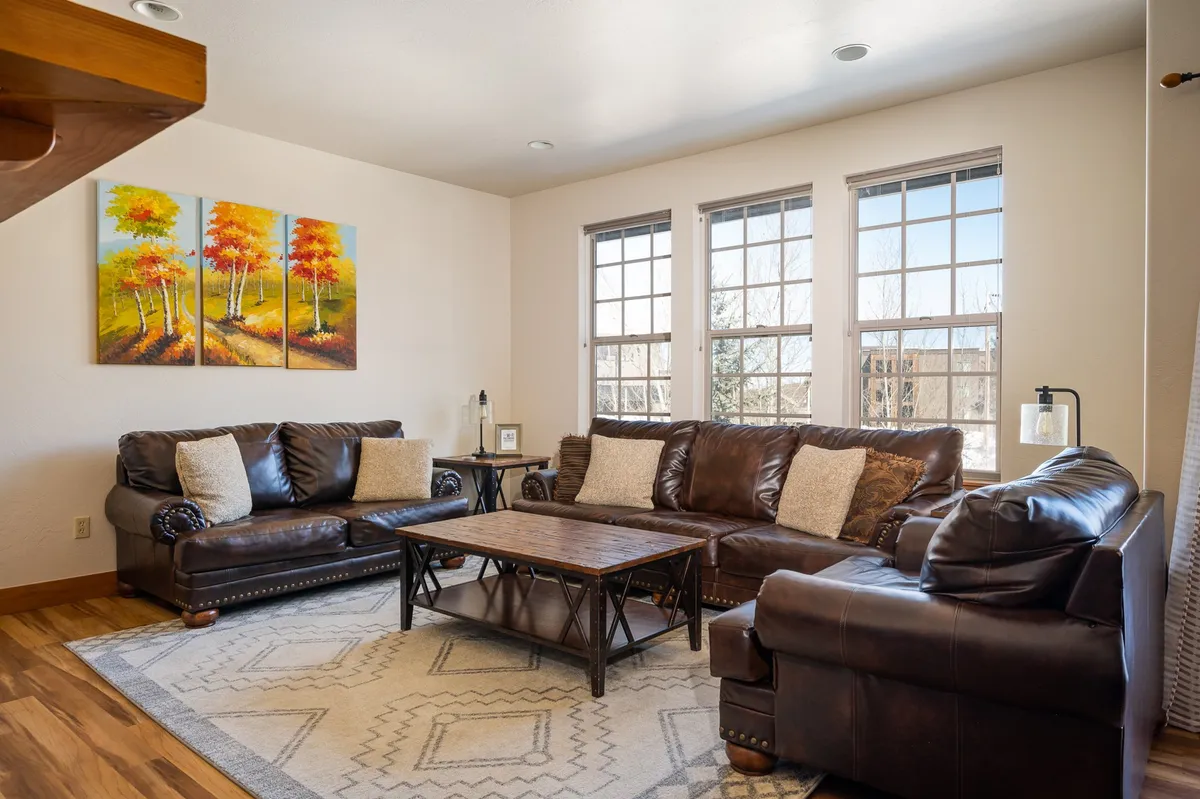 The image shows a warm and spacious living area with leather sofas arranged around a wood coffee table. Artwork on the wall adds character, while soft lighting and comfortable seating create an inviting atmosphere ideal for socializing and relaxation.